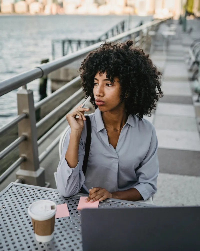 Woman with pen and coffee working outdoors, maintaining sharp mental focus and clarity