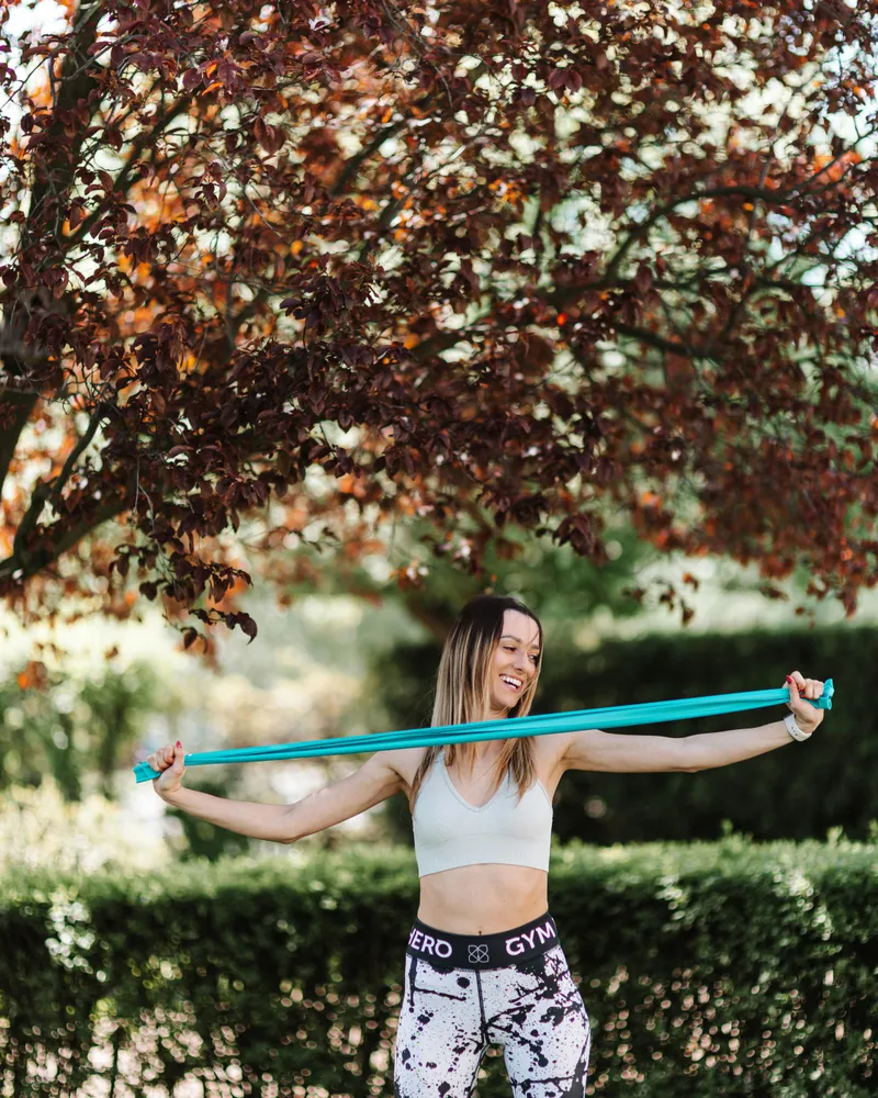 Smiling woman using a resistance band outdoors as part of an active injury recovery and rehabilitation routine