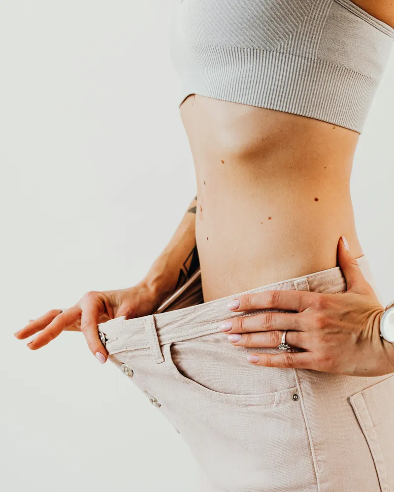 Fit woman showing her weight loss progress in oversized jeans