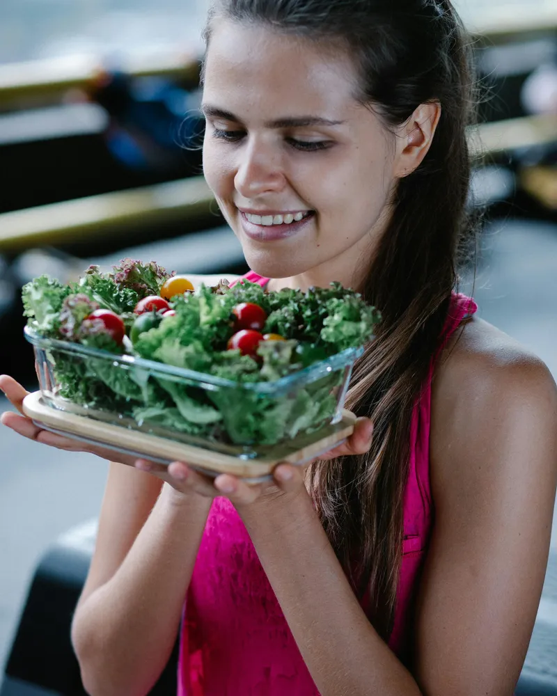 Smiling woman in a pink top holding a fresh salad bowl, embracing a healthy lifestyle